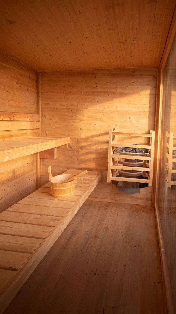 Inside the cedar sauna, with tiered bench seating and a wooden water bucket.